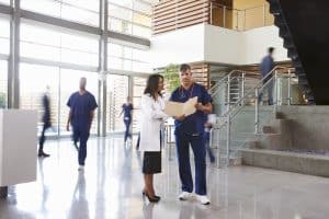 Two healthcare workers talk in the lobby of a busy hospital